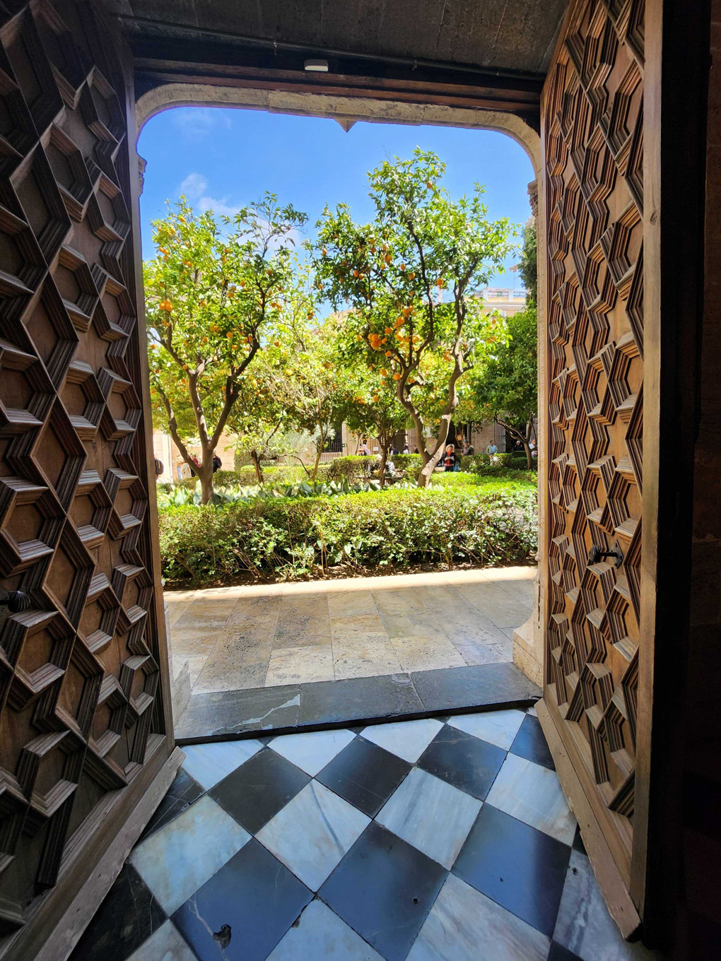 Two large and ornate doors are open, leading to a courtyard full of orange trees.