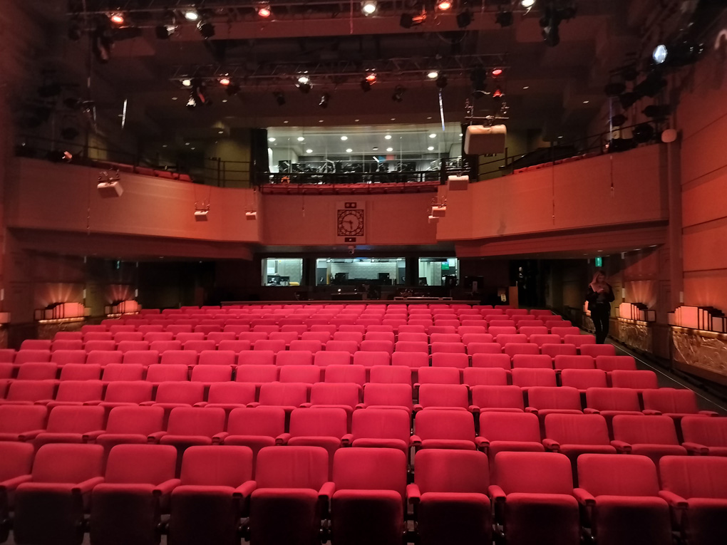 The interior of the BBC Radio Theatre as seen from the stage. About 200 empty red seats and a control room at the back.