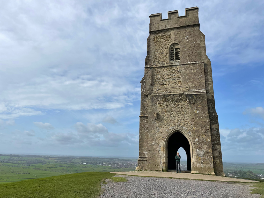 The tower of a old church on a huge hill with a blue sky and clouds behind