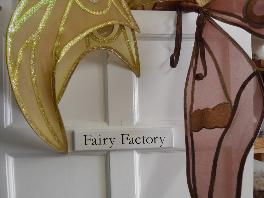 Costume wings hanging on a door labelled Fairy Factory