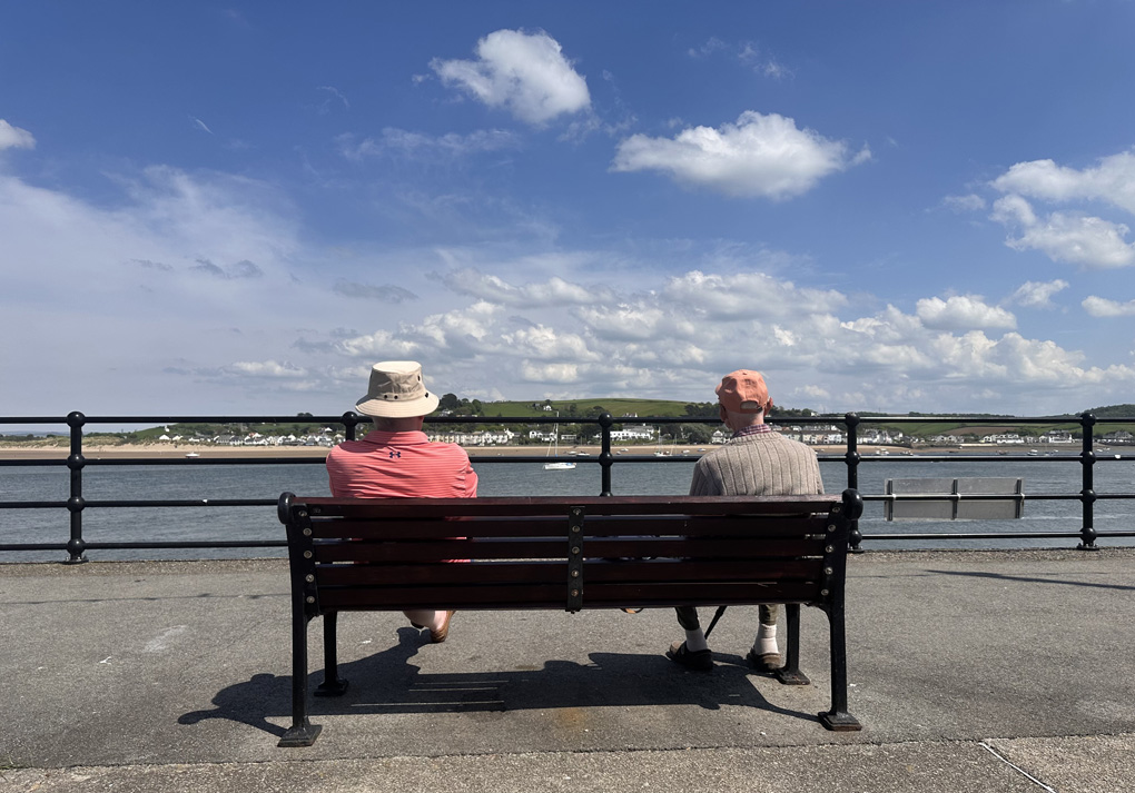 Two men sat on a bench looking out over an estuary