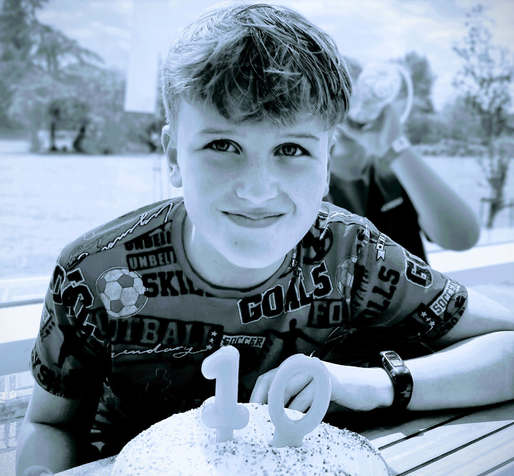 Joshua staring intently into the camera, with a cake on the table under him. There are candles for his 10th birthday!