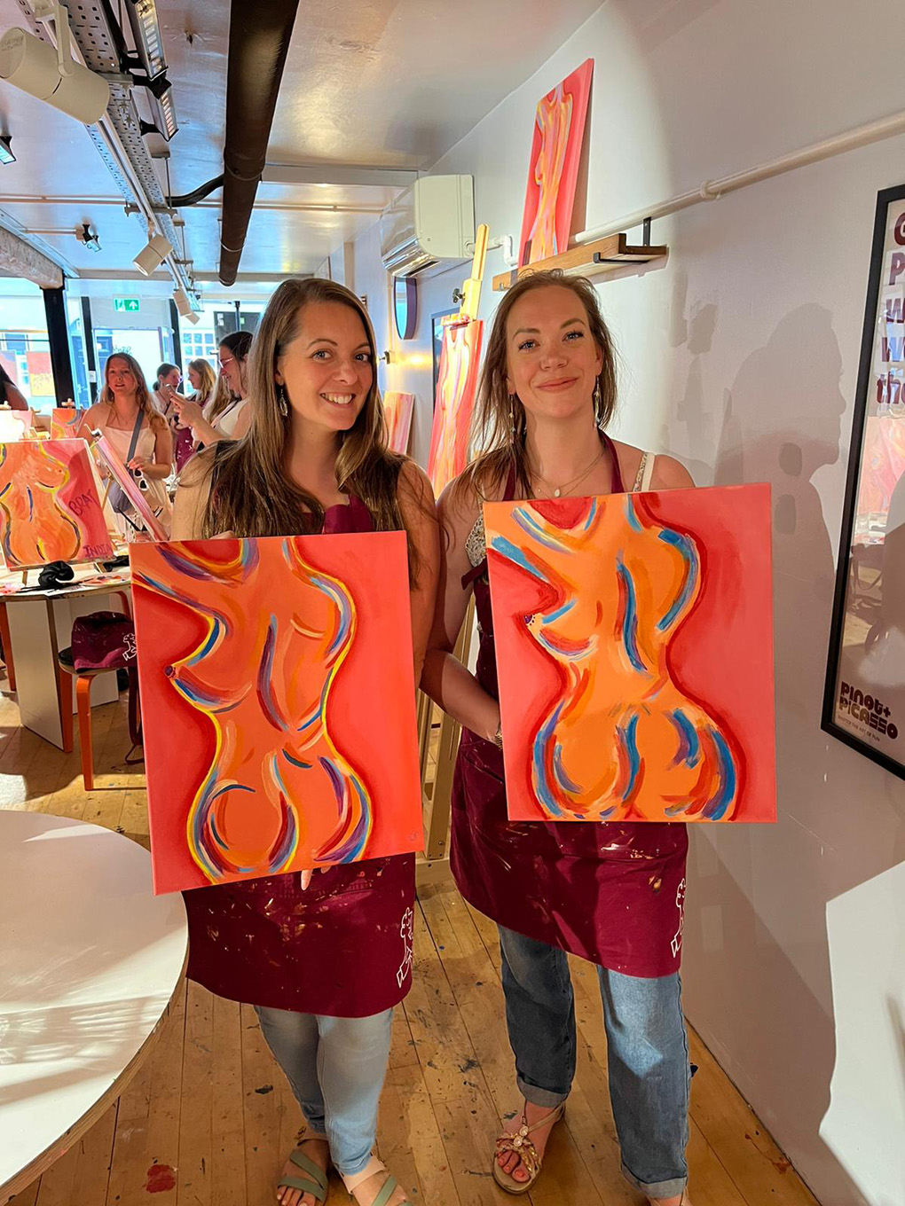 Two ladies holding paintings of the female form