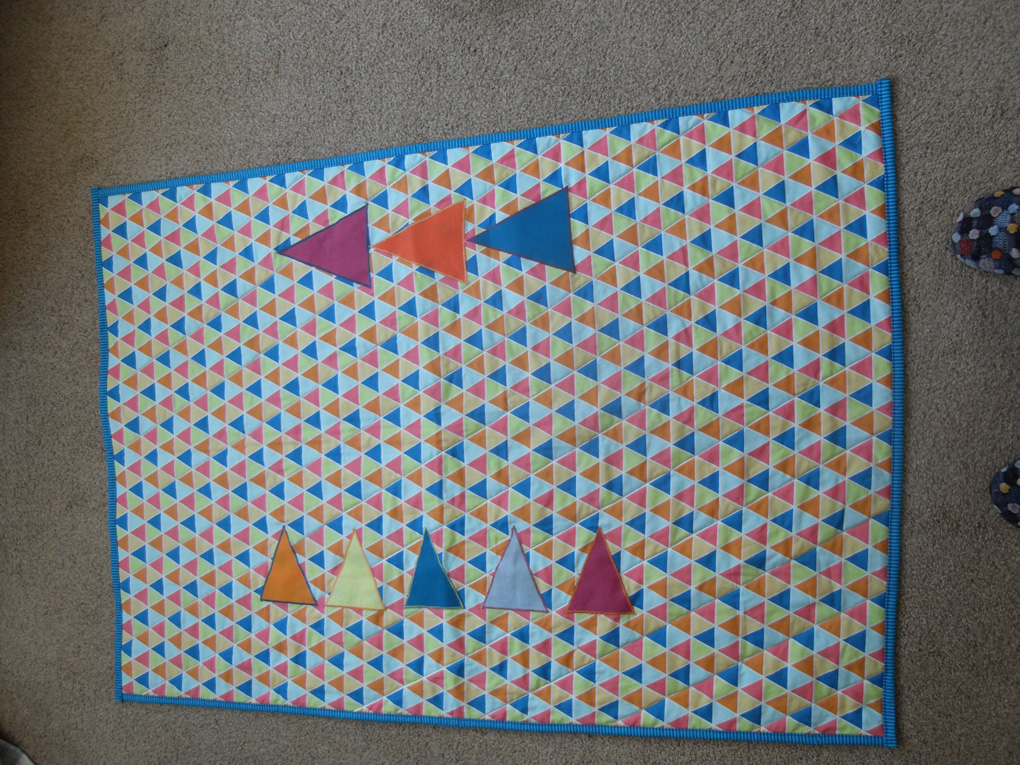 Multi coloured cot quilt featuring triangles.