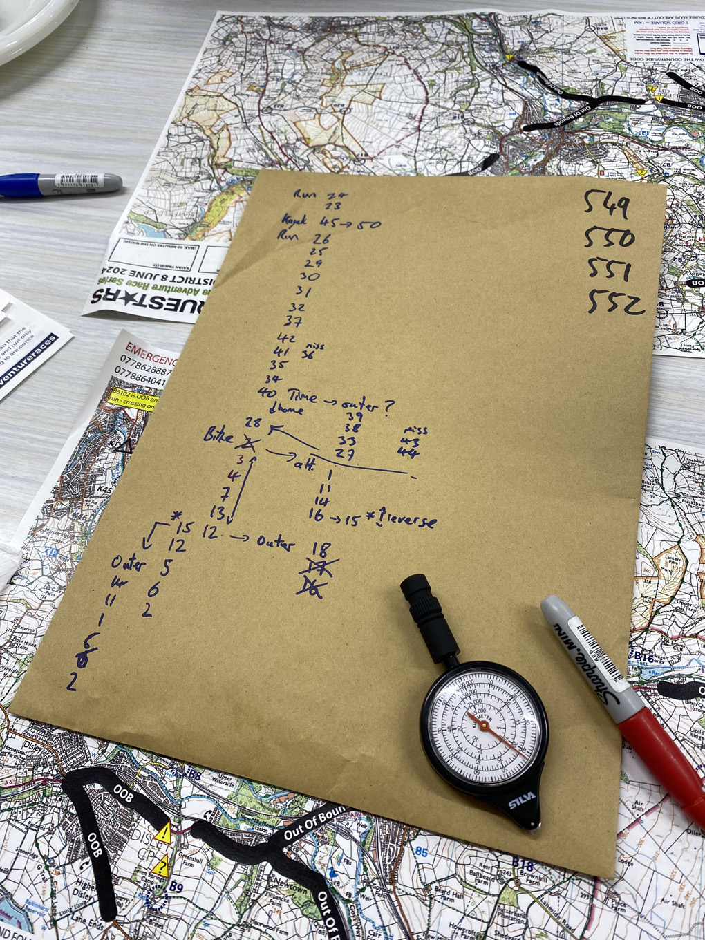 A brown envelope with a list of numbers and arrows, planning out routes between checkpoints. Marked-up Ordnance Survey maps sit under the eenvelope.