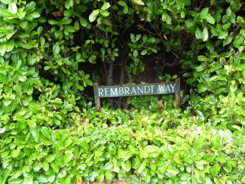 Rectangular hole cut in hedge so street nameplate can be read.