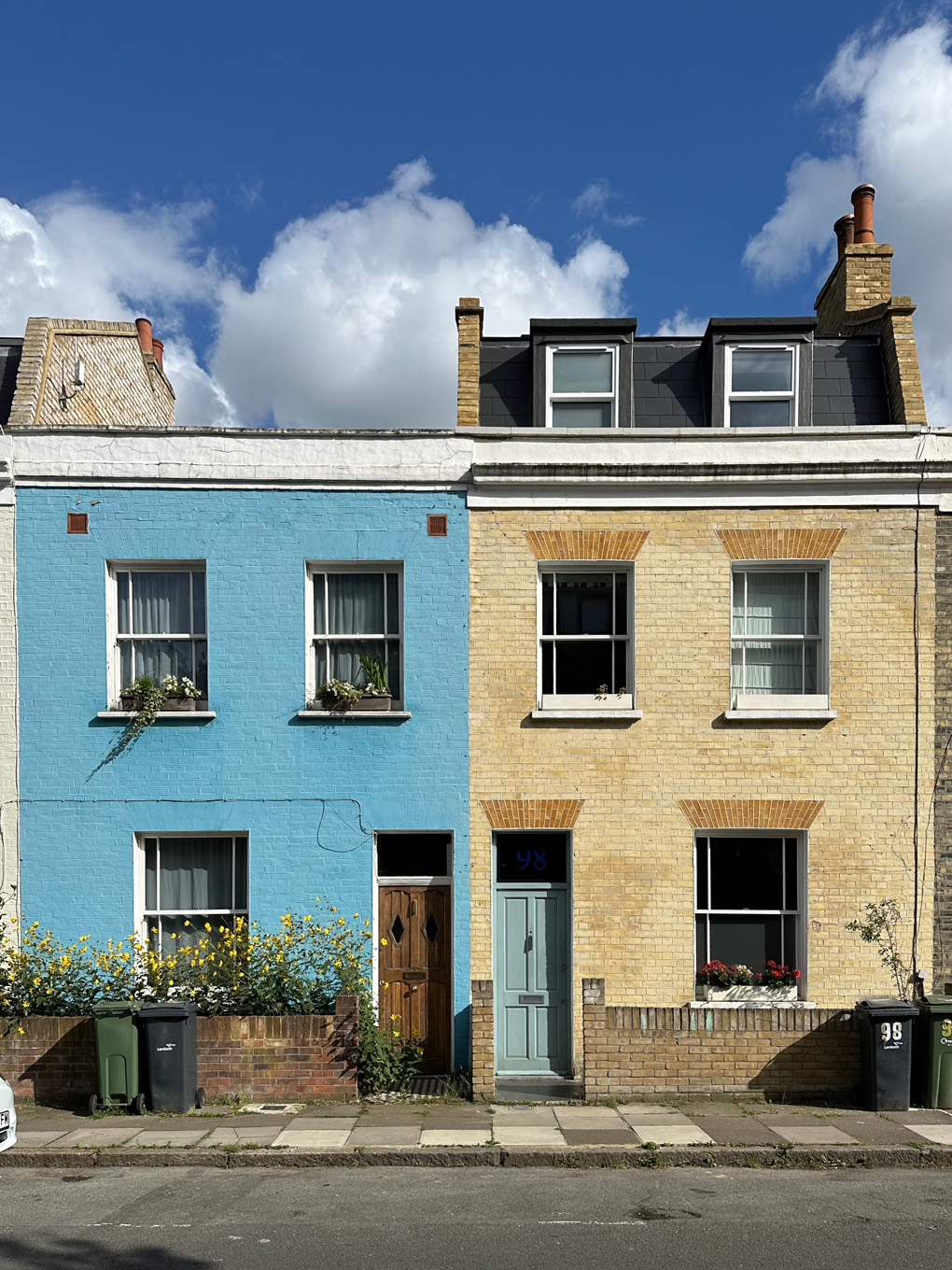 Couple of terraced houses. One on left painted light blue. Blue sky with some clouds above.