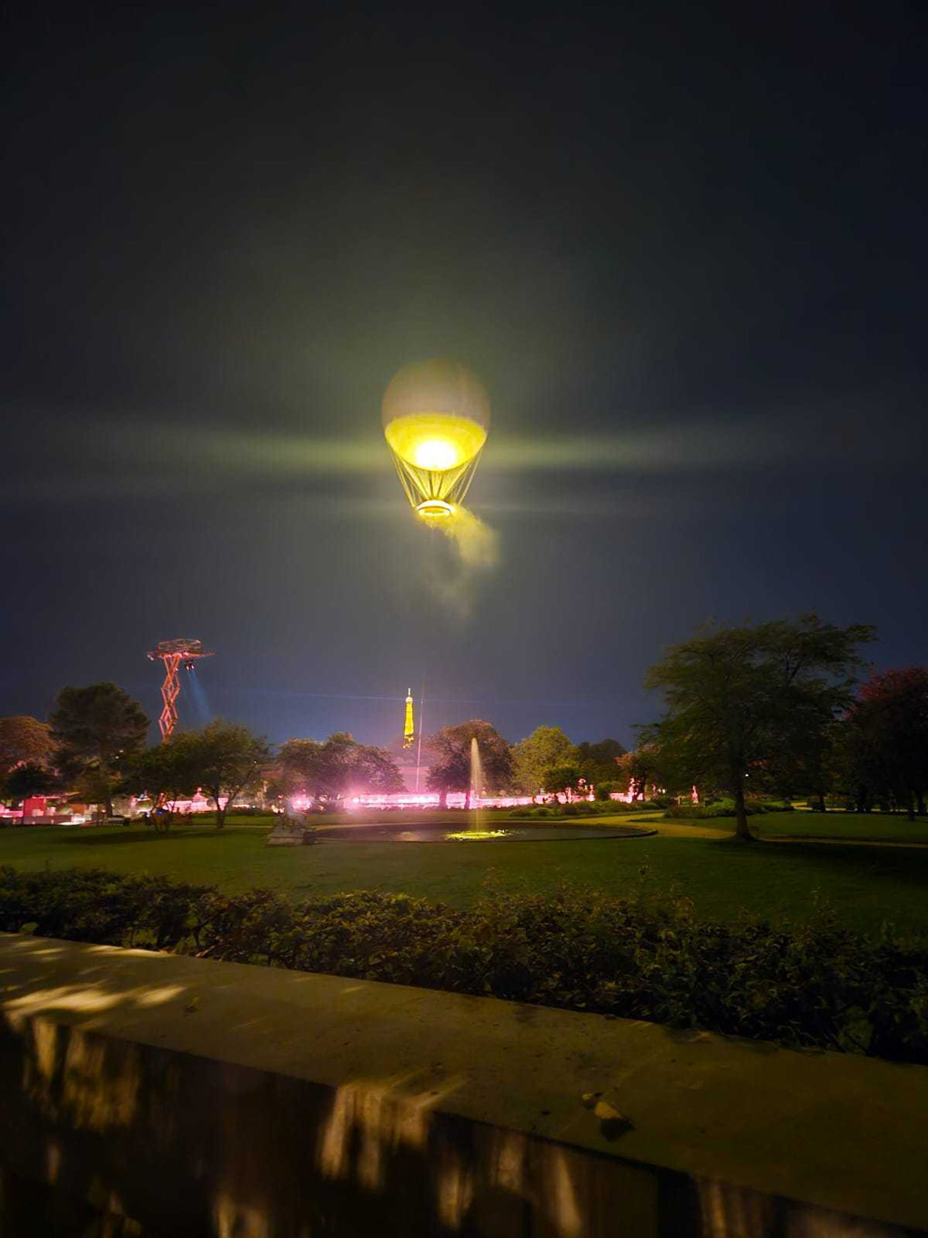 The paralympic flame powers a white hot air balloon and is illuminated in the night sky. It hovers near the effiel tower whichis lit up in gold