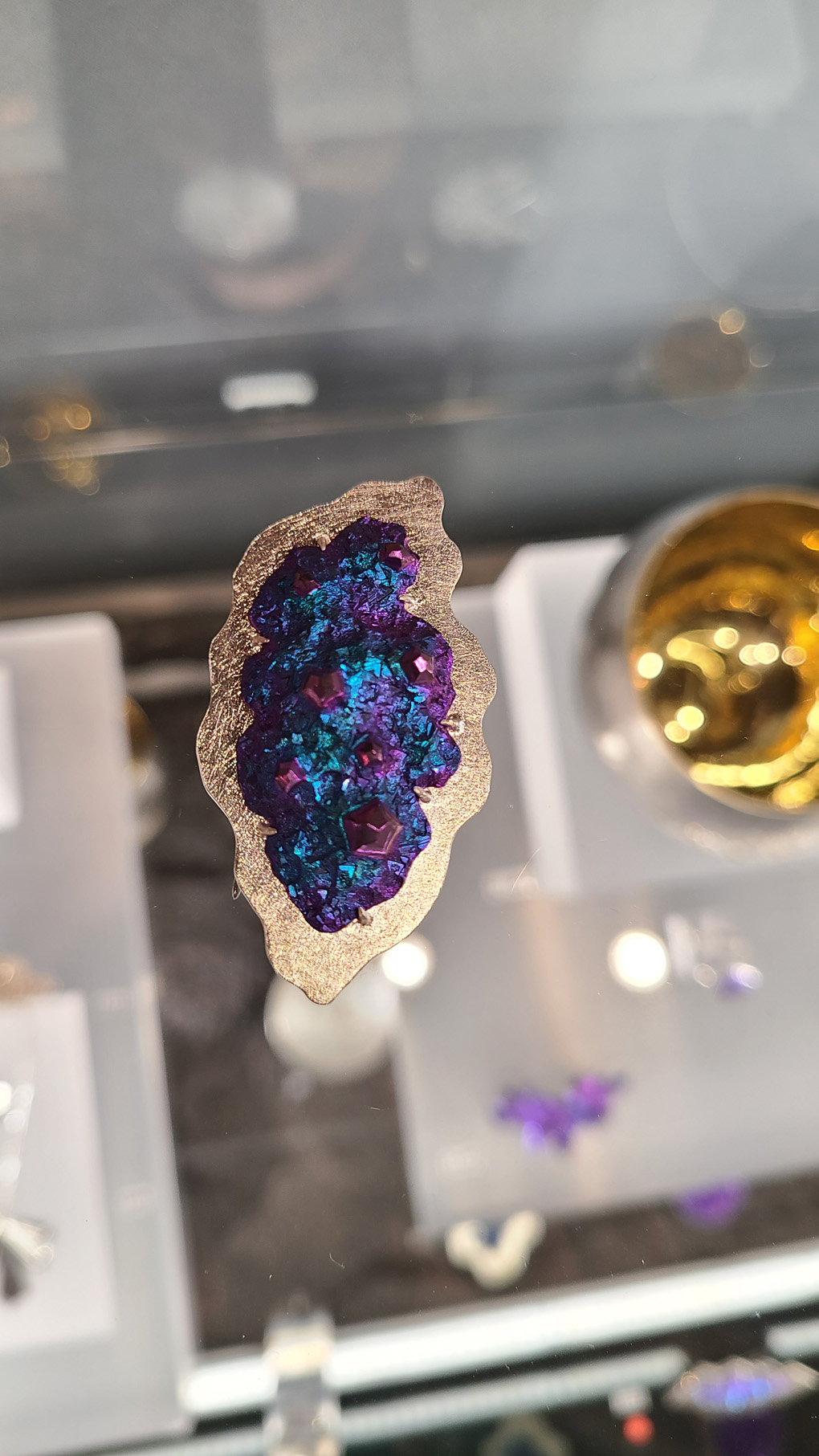 A sterling silver and purple/blue niobium brooch on a glass display cabinet.