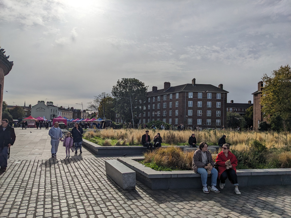 If you turn your back on the river in Greenwich by the Cutty Sark there is an open area with raised reed beds and benches for sitting and watching the Thames. There's the colourful tents of a food fair in the distance and a week autumn sun shining through a wide open sky of cloud