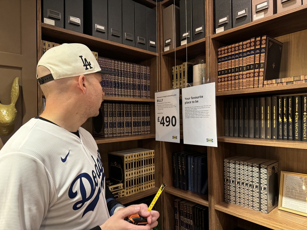 Man in baseball cap with measuring tape next to bookshelves for sale