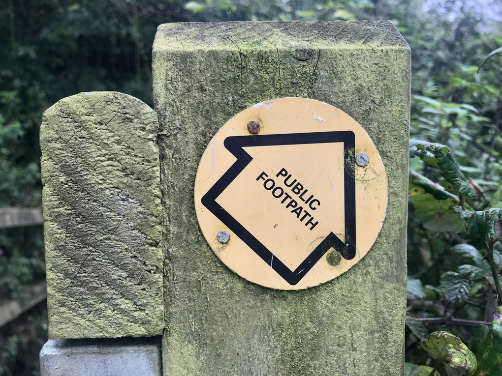 Country fence post with round yellow public footpath sign