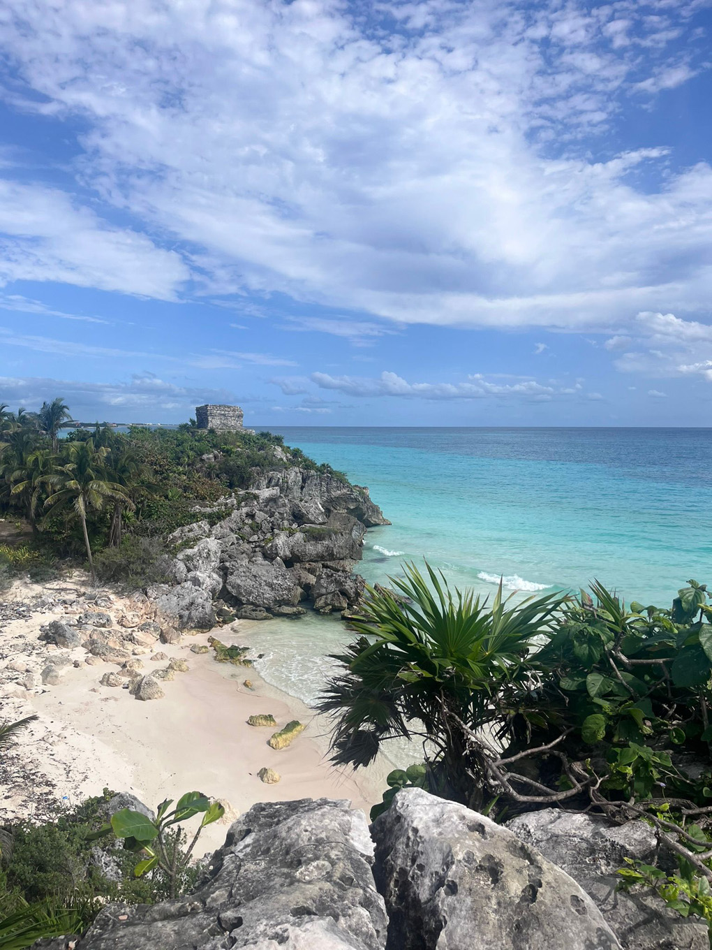 A Mayan ruin in the distance, on a cliff next to the beach and sea