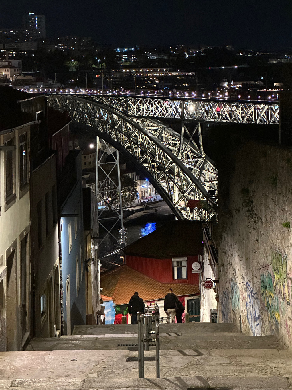 Steps leading down and a lit up two level bridge in distance at night. River visible beneath.