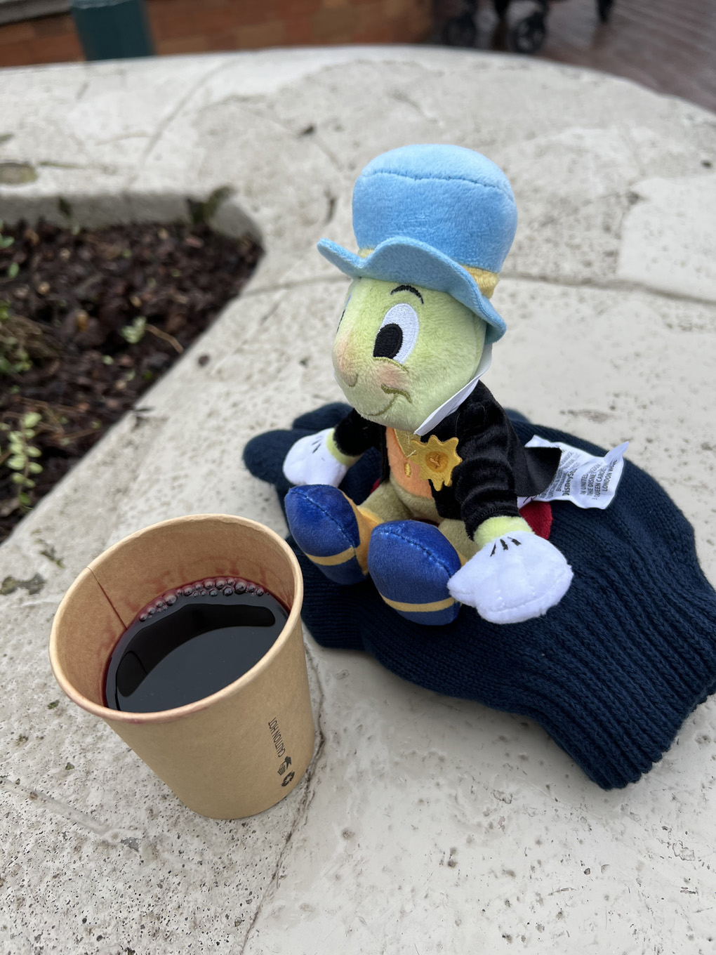 Jiminy cricket toy on glove next to cup of red wine