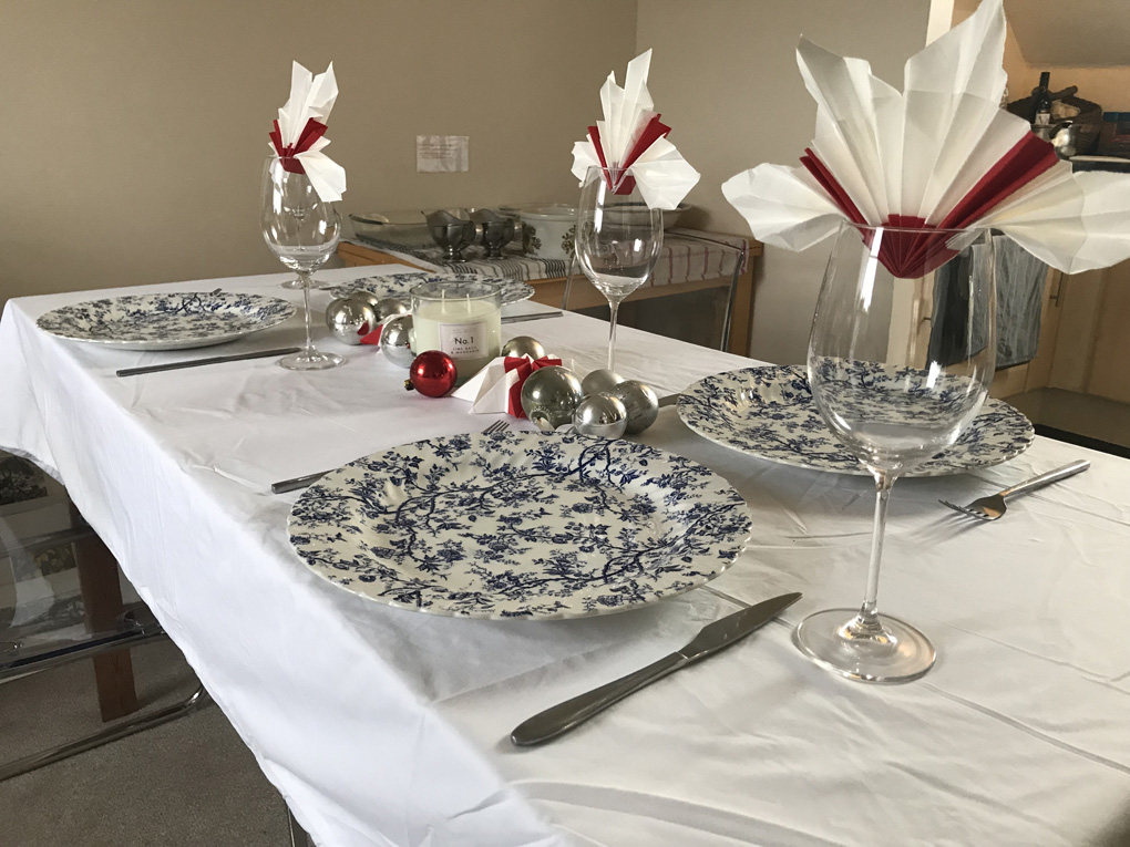 Dinning table with white table cloth, blue and white plates, wine glasses holding red and white napkins.