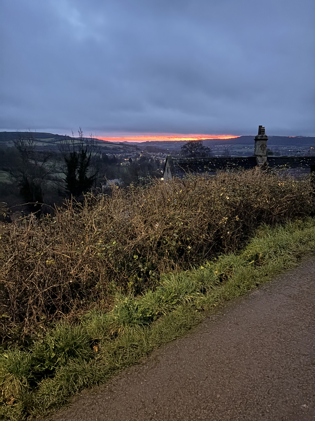 Looking out across the countryside outside of Bath. In the far distance there is a glowing red and orange sunrise on the horizon