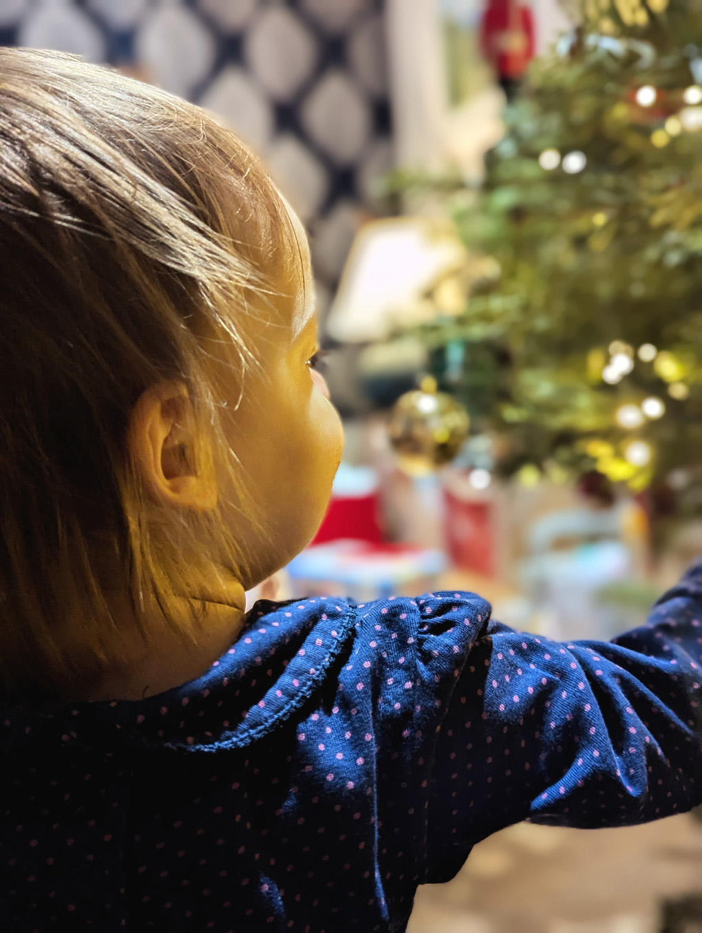 A toddler looking at a Christmas tree (out fo focus). The light reflect off her face creating a warm glow