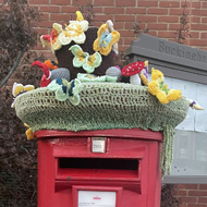 Red Royal Mail post box with a knitted topper.