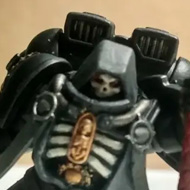 A Warhammer miniature painted in blacks, whites and greys stands poised on a stone, as if descending to smite his foe