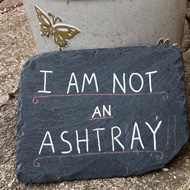 A sign that reads ‘I am not an ashtray’ is propped up against a sad looking tree in a ceramic pot