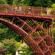 Half of the rusty looking bridge set against verdant green of the trees and faintly reflected in the moving waters of the River Severn