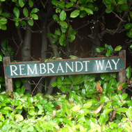 Rectangular hole cut in hedge so street nameplate can be read.