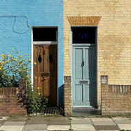 Couple of terraced houses. One on left painted light blue. Blue sky with some clouds above.