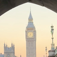 Big Ben and Westminster Bridge at sunset through an arch with people passing by.