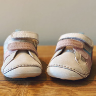 A pair of pink and white first trainers for baby girl with velcro straps