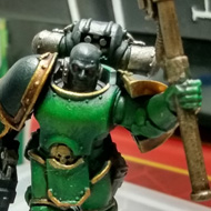 A green armoured space marine holds his hammer aloft surrounded by the tat on my desk