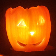 An orange pepper with a face carved into it. A candle inside illuminates it as it looks out a dark window