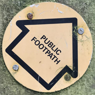 Country fence post with round yellow public footpath sign