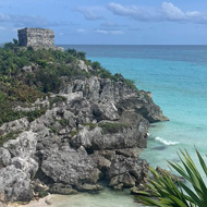 A Mayan ruin in the distance, on a cliff next to the beach and sea