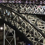 Steps leading down and a lit up two level bridge in distance at night. River visible beneath.