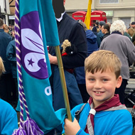 Jack holding the Beavers flag in a crowd of people before the start of the remembrance day parade. Big smiles all around!