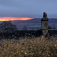 Looking out across the countryside outside of Bath. In the far distance there is a glowing red and orange sunrise on the horizon