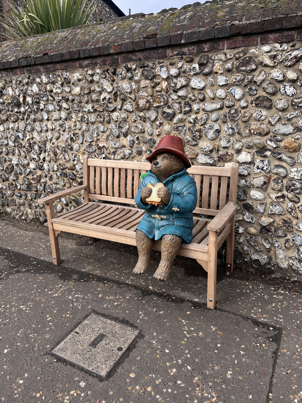 A statue of Paddington Bear sitting on a bench eating a marmalade sandwich