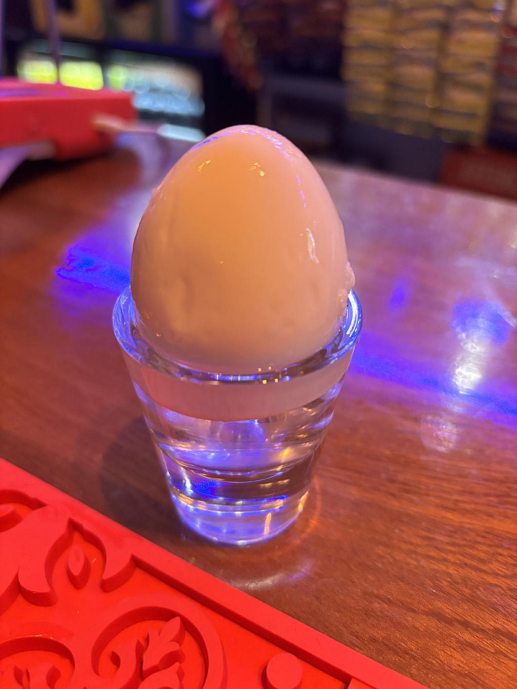 A pickled egg sat in a small glass on a wooden pub bar