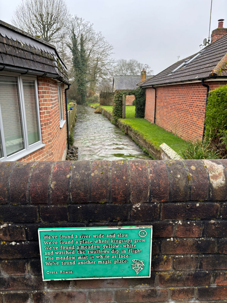 A plaque on a road bridge display the following poem by Greta Rowse...We've found a river wide and slow  We've found place where kingcups grow  We've found a meadow yellow-white  and watched the swallows dip in flight  The meadow mist is white as lace We've found another magic. Unfortunately the view over the bridge is of a stream channeled between  the backs of modern buildings.