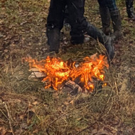 Numerous warmly attired villagers gathered around a bonfire in the cold woods with a dram of whisky for a neighbourly blether