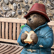 A statue of Paddington Bear sitting on a bench eating a marmalade sandwich