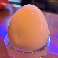 A pickled egg sat in a small glass on a wooden pub bar