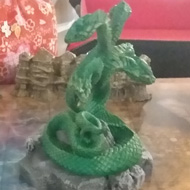 A green painted, 5-headed snake miniature stands next the edge of an underground lake