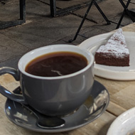 View from a table outside at a cafe next to Bath Abbey. The sun is shining, there is a plate with pastries on the table and beyond the tables there is the front of the Abbey.